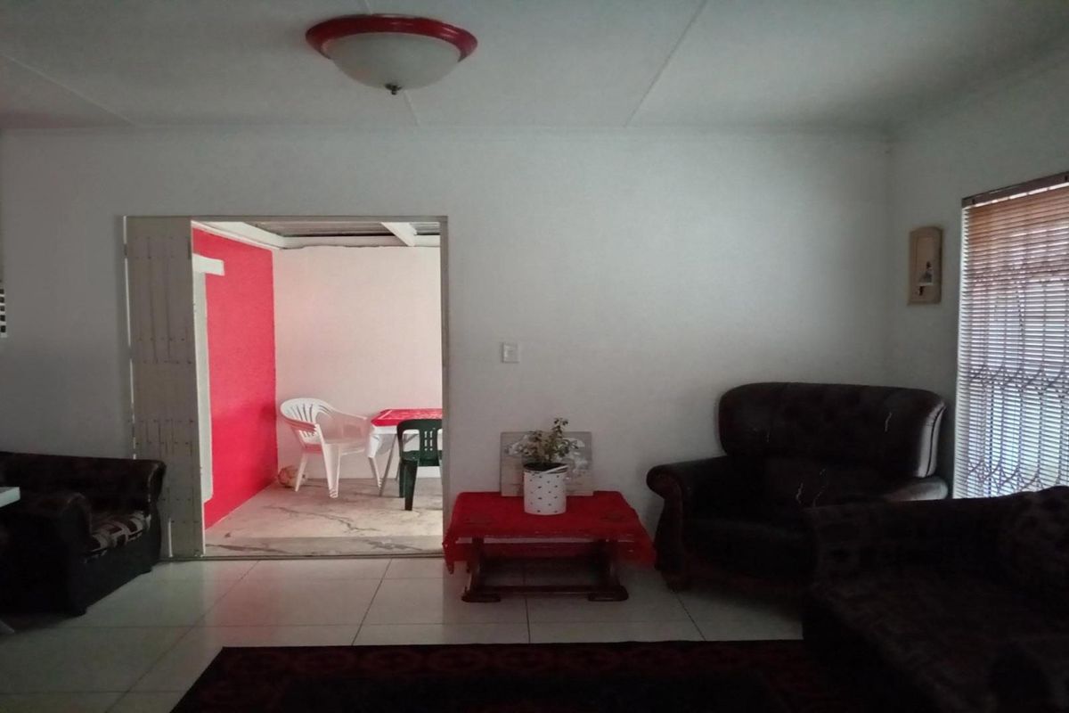 A living room area featuring tiled flooring and a ceiling light fixture, with an adjacent room visible through a doorway.