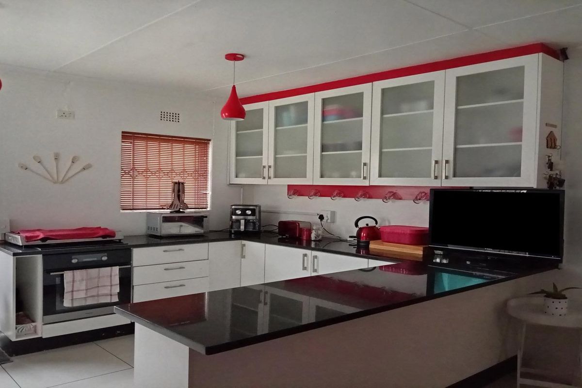 A functional kitchen featuring white cabinetry, contrasting black granite countertops, built-in oven, and modern red pendant lighting.