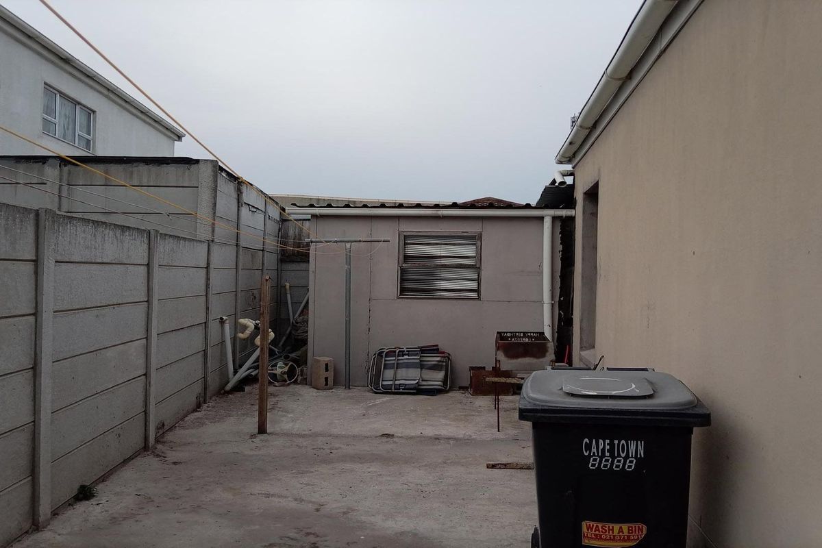 A functional rear exterior area featuring concrete paving, boundary walls, and a small utility structure, offering potential for landscaping or outdoor improvement.