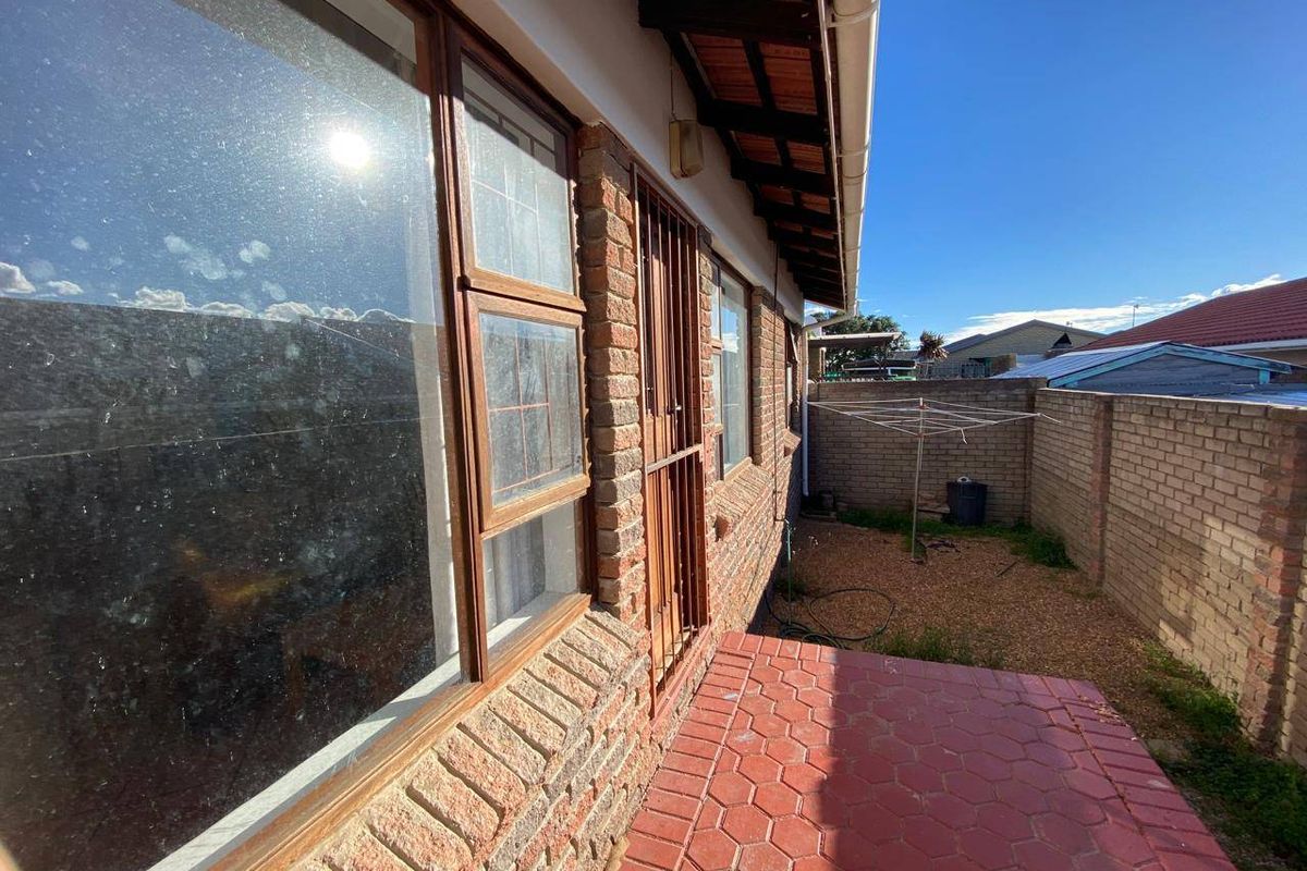Rear exterior view of the property featuring a brick facade, tiled patio area, and a secure boundary wall.