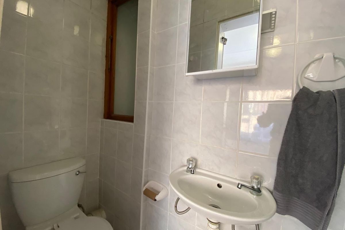 A compact bathroom featuring white wall tiles, a wall-mounted basin, a toilet, and a medicine cabinet with a timber-framed window.