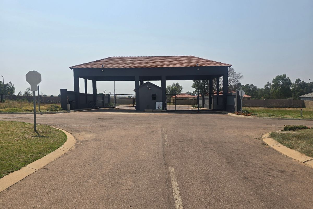 A secure gated entrance to the residential estate featuring a covered guardhouse and paved access road.
