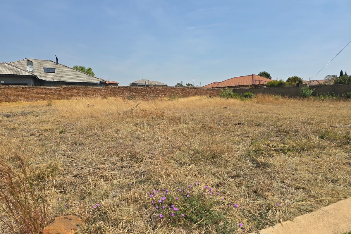 A vacant residential plot featuring dry grass and perimeter brick boundary walls, offering a clear space ready for development.