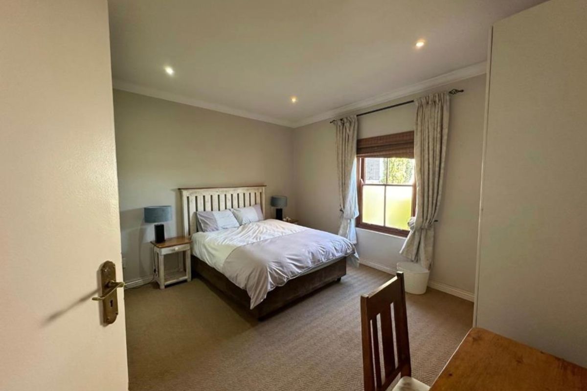 A well-maintained bedroom featuring neutral walls, carpeted flooring, recessed downlighting, and a window with fitted curtains.