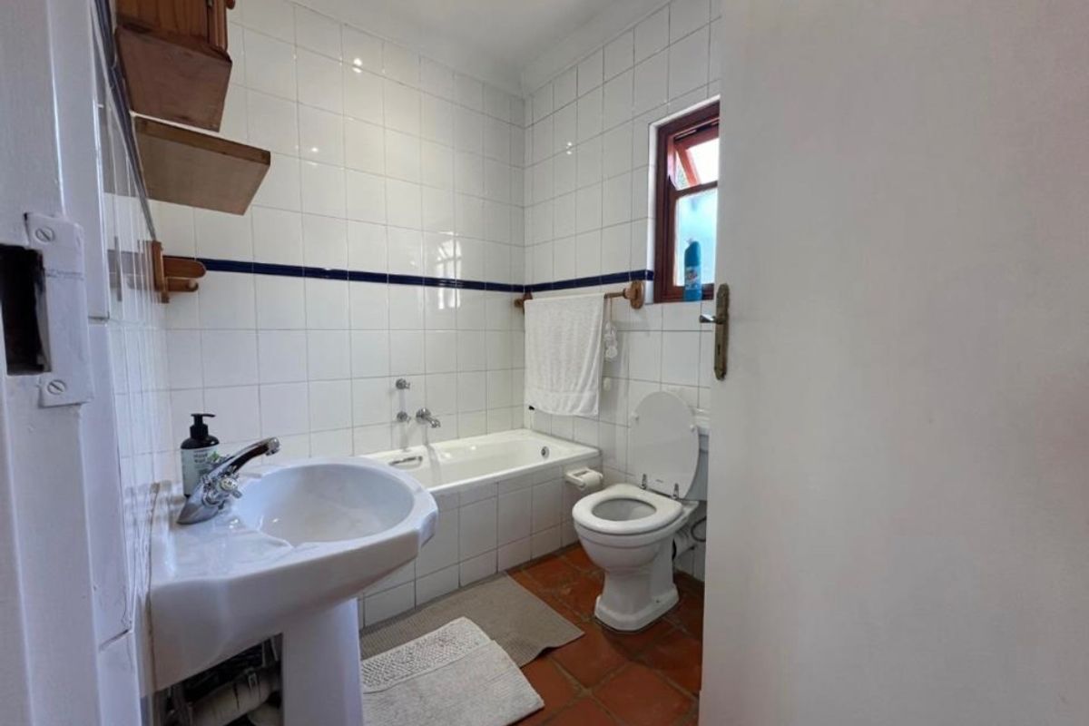 A functional bathroom featuring a pedestal basin, bathtub, and toilet with classic white wall tiles and terracotta floor tiling.