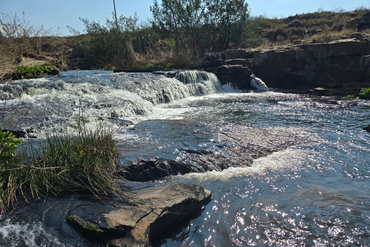 A scenic view of a natural waterfall and rocky stream flowing through the vacant residential land.