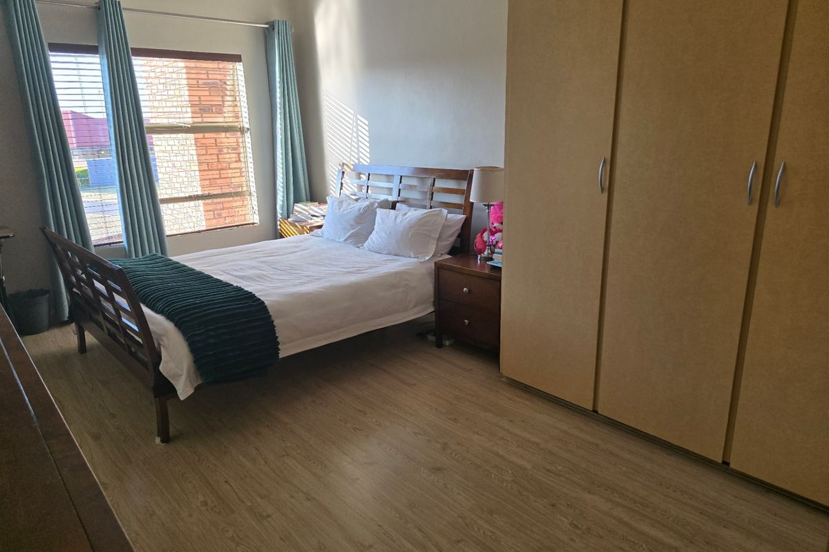 A bedroom featuring light wood-look laminate flooring and a large built-in wardrobe with light-toned doors.