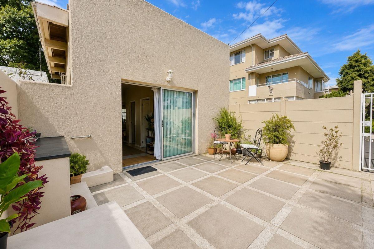 A private rear patio area featuring paved flooring, a sliding glass door entrance, and a perimeter boundary wall.