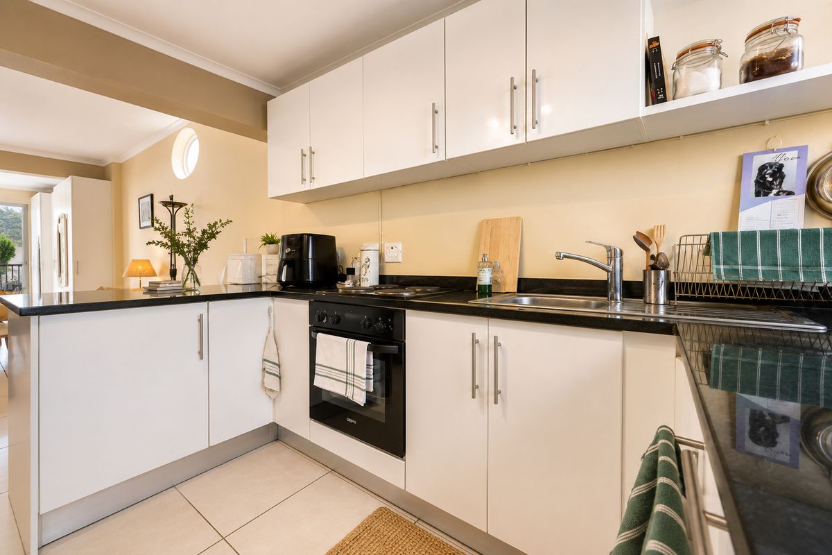 A modern kitchen featuring white cabinetry, black stone countertops, a built-in oven, and a stainless steel sink with a mixer tap.