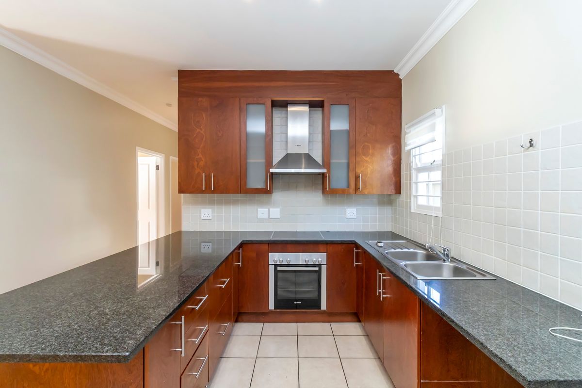 A functional kitchen featuring dark wood cabinetry, granite countertops, a built-in oven, stainless steel extractor fan, and a double bowl sink.