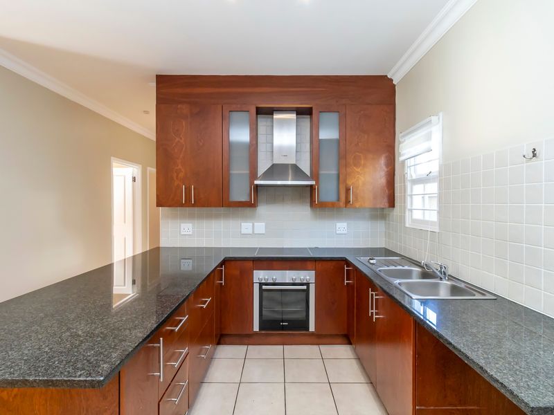 A functional kitchen featuring dark wood cabinetry, granite countertops, a built-in oven, stainless steel extractor fan, and a double bowl sink.