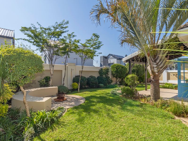 A well-maintained private garden featuring a landscaped lawn, a built-in curved bench, and a covered patio area perfect for outdoor relaxation.