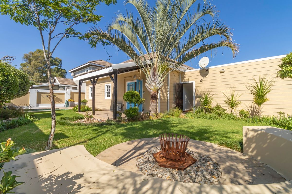 A well-maintained rear garden featuring a covered patio with timber pergola, landscaped lawn, and a dedicated fire pit area.