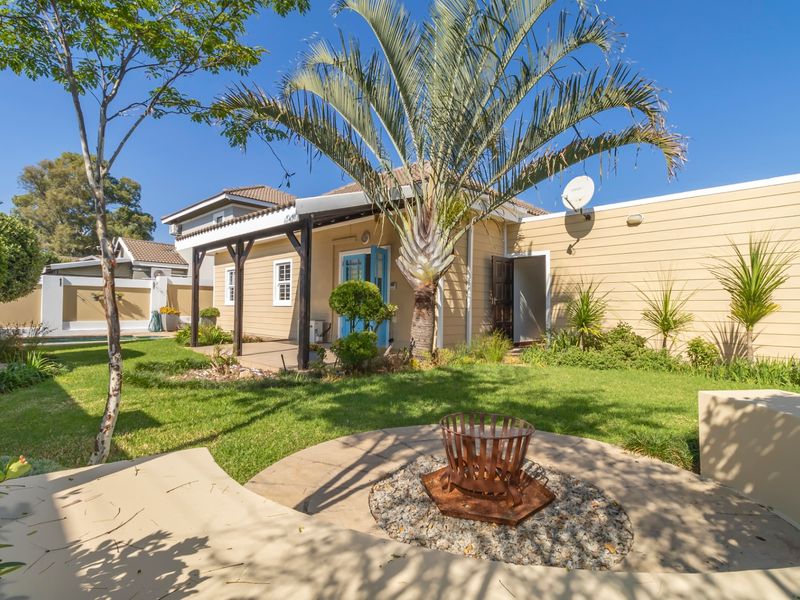 A well-maintained rear garden featuring a covered patio with timber pergola, landscaped lawn, and a dedicated fire pit area.