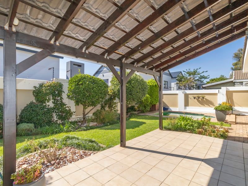 A covered patio area featuring a timber pergola, tiled flooring, and direct access to a landscaped garden and swimming pool.