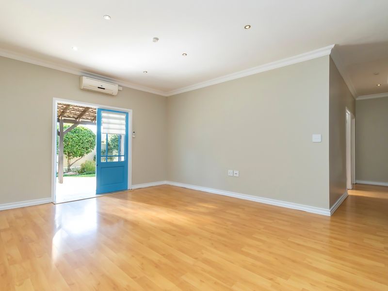 A bright, empty living room featuring laminate flooring, recessed lighting, and direct access to an outdoor patio area through a blue door.