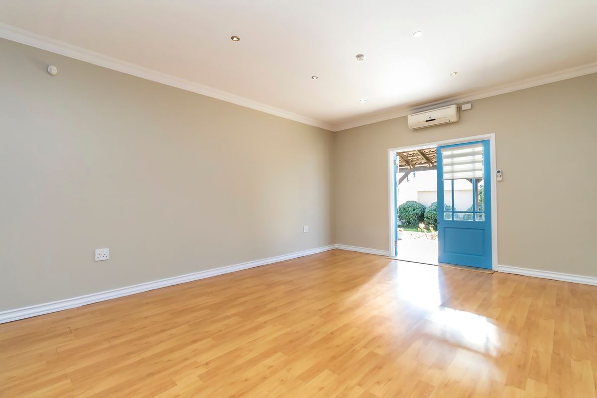 A bright, empty living room featuring laminate flooring, recessed downlighting, and a split-system air conditioner, with direct access to an outdoor patio area.