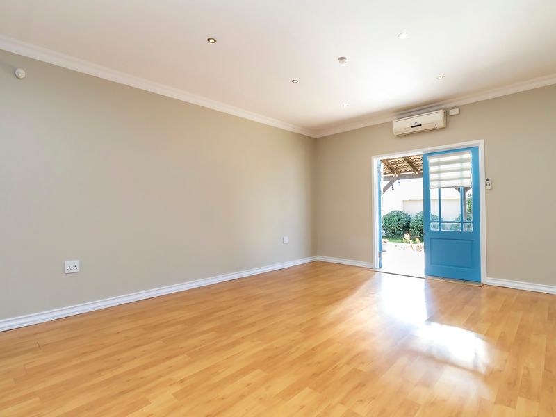 A bright, empty living room featuring laminate flooring, recessed downlighting, and a split-system air conditioner, with direct access to an outdoor patio area.