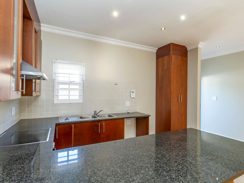 A clean, well-maintained kitchen featuring dark granite countertops, warm wooden cabinetry, a stainless steel sink, and a built-in extractor fan.