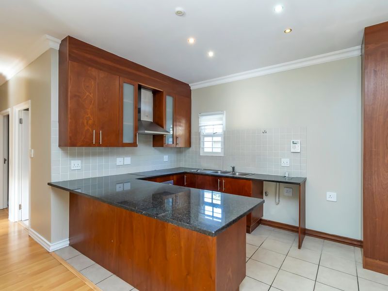 A clean and functional kitchen featuring dark wood cabinetry, granite countertops, a stainless steel extractor fan, and neutral tiled flooring.