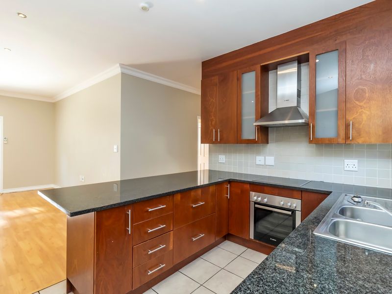 A functional kitchen featuring dark granite countertops, wooden cabinetry, built-in oven, electric cooktop, and a stainless steel extractor fan, adjacent to an open living area.