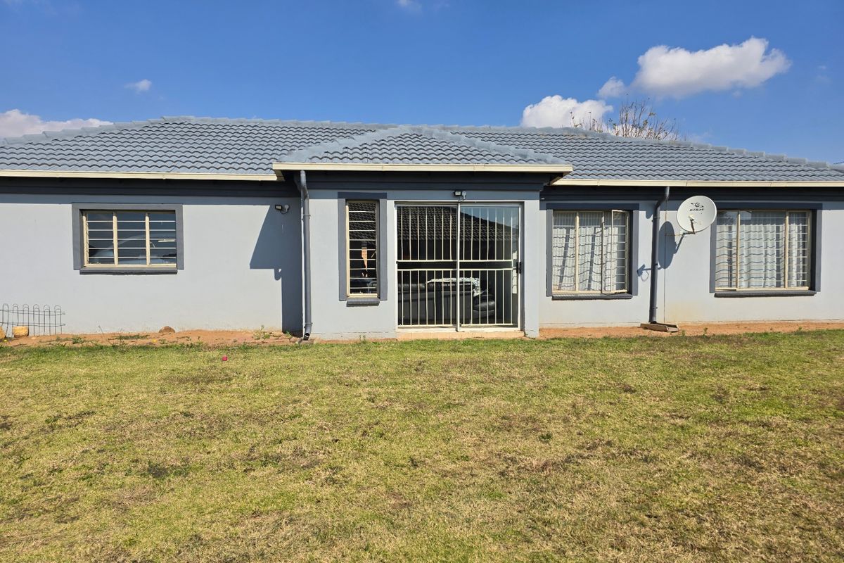 Rear view of the house featuring a tiled roof, sliding glass door with security gate, and multiple windows with security bars.