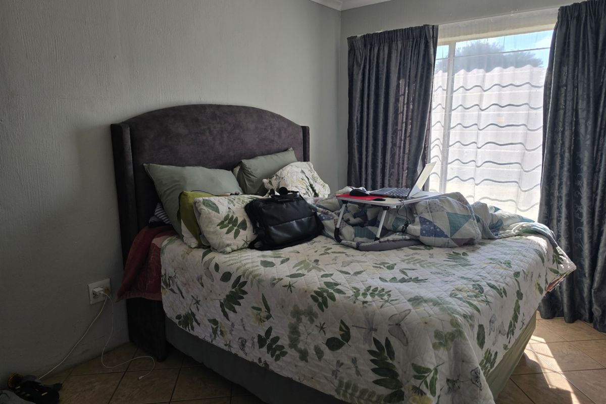 A bedroom featuring tiled flooring and a window with curtains, providing natural light to the space.