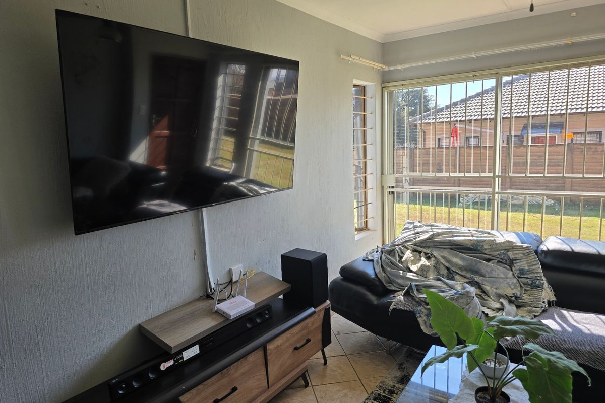 A living room featuring tiled flooring, large windows with security bars, and a wall-mounted television setup.