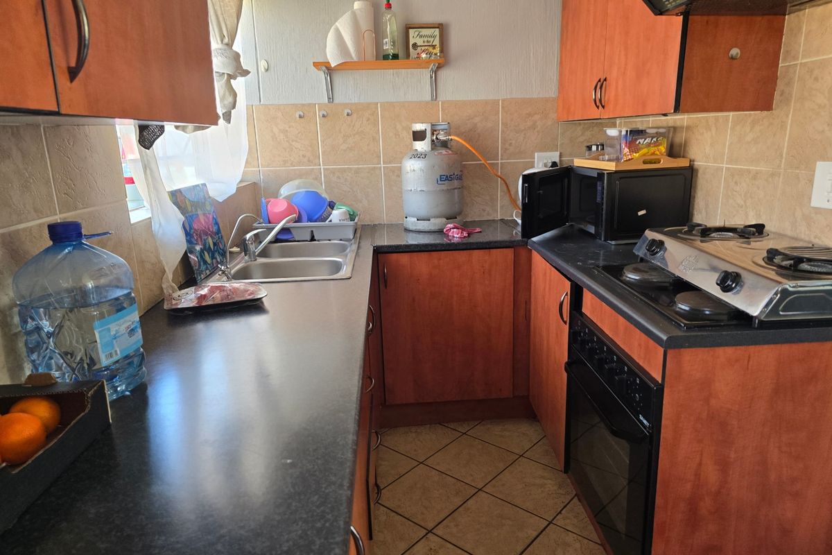 Compact kitchen featuring dark laminate countertops, wooden cabinetry, a built-in oven with gas hob, and a double stainless steel sink.