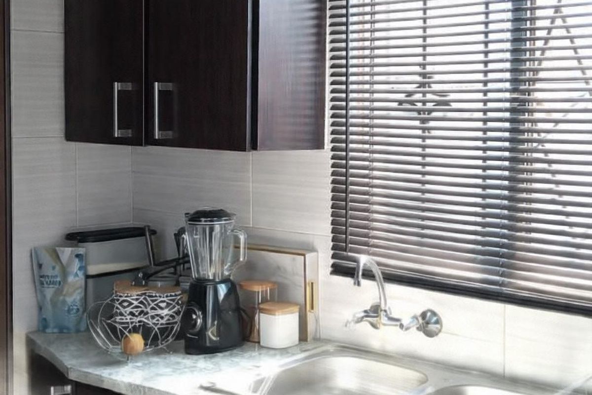 A functional kitchen area featuring dark wood cabinetry, a double stainless steel sink, stone-look countertops, and horizontal window blinds.