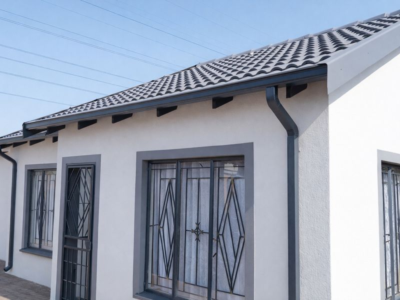 A well-maintained exterior view of the house featuring modern tiled roofing, clean white rendered walls, and secure metal window and door grilles.