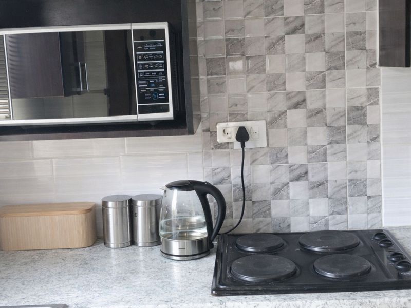 A functional kitchen area featuring dark wood cabinetry, a built-in oven with electric hob, a microwave, and a tiled backsplash.