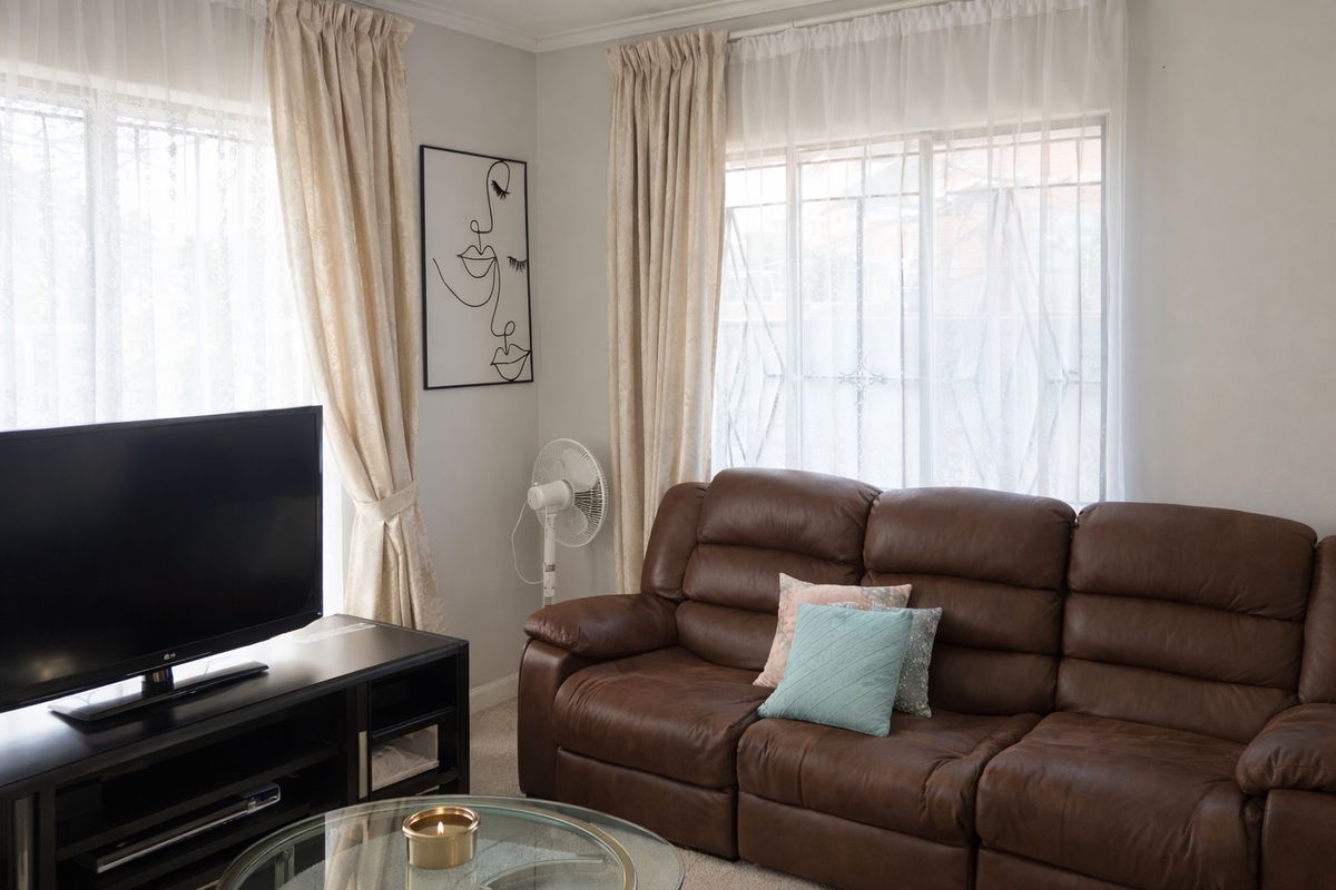 A comfortable living room featuring large windows with curtains and neutral wall finishes, providing a bright and functional space for relaxation.