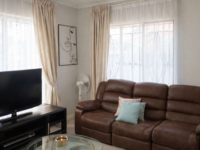 A comfortable living room featuring large windows with curtains and neutral wall finishes, providing a bright and functional space for relaxation.