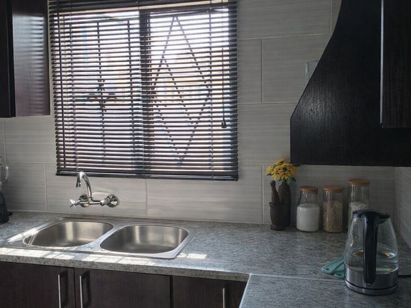 A functional kitchen area featuring a double stainless steel sink, granite-look laminate countertops, tiled backsplash, and a dark wood-finish extractor fan.