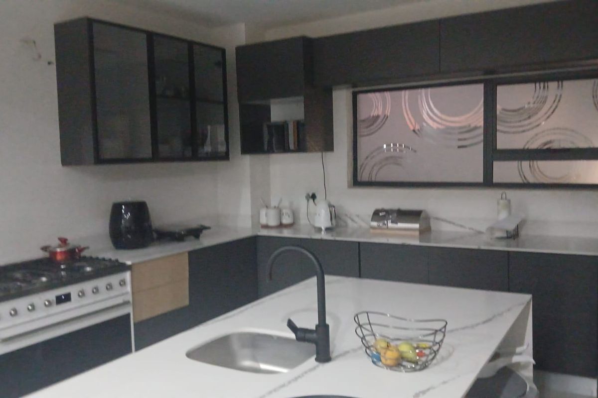 Modern kitchen featuring dark cabinetry, stone countertops, a central island with a sink, and a built-in gas stove.