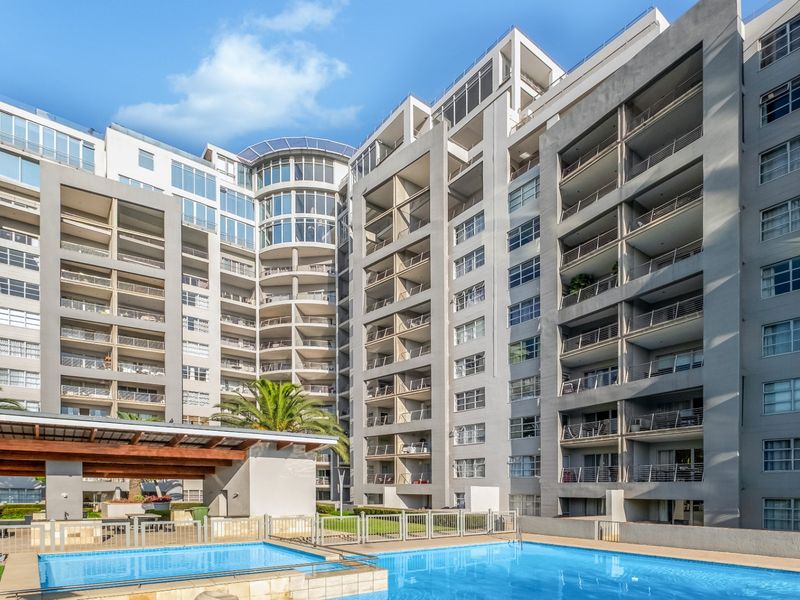 A view of the apartment complex exterior featuring a swimming pool, landscaped garden areas, and multiple levels of private balconies.