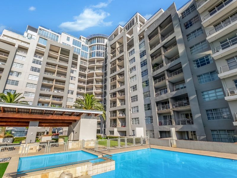 A view of the apartment complex exterior featuring a swimming pool area with a covered patio structure and landscaped surroundings.