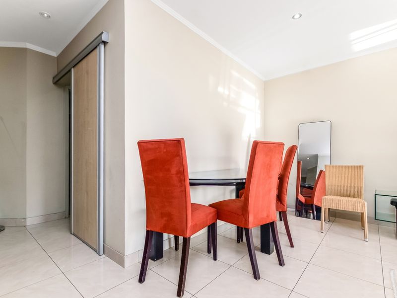 A bright dining area featuring neutral tiled flooring, recessed ceiling lighting, and a modern sliding door leading to an adjacent space.