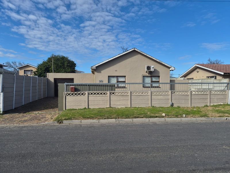 Front exterior view of a single-story house featuring a paved driveway, secure boundary wall, and an installed air conditioning unit.