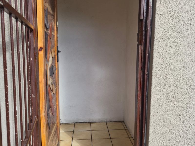An entrance area featuring a decorative wooden door, a metal security gate, and tiled flooring, showing signs of wear and weathering.