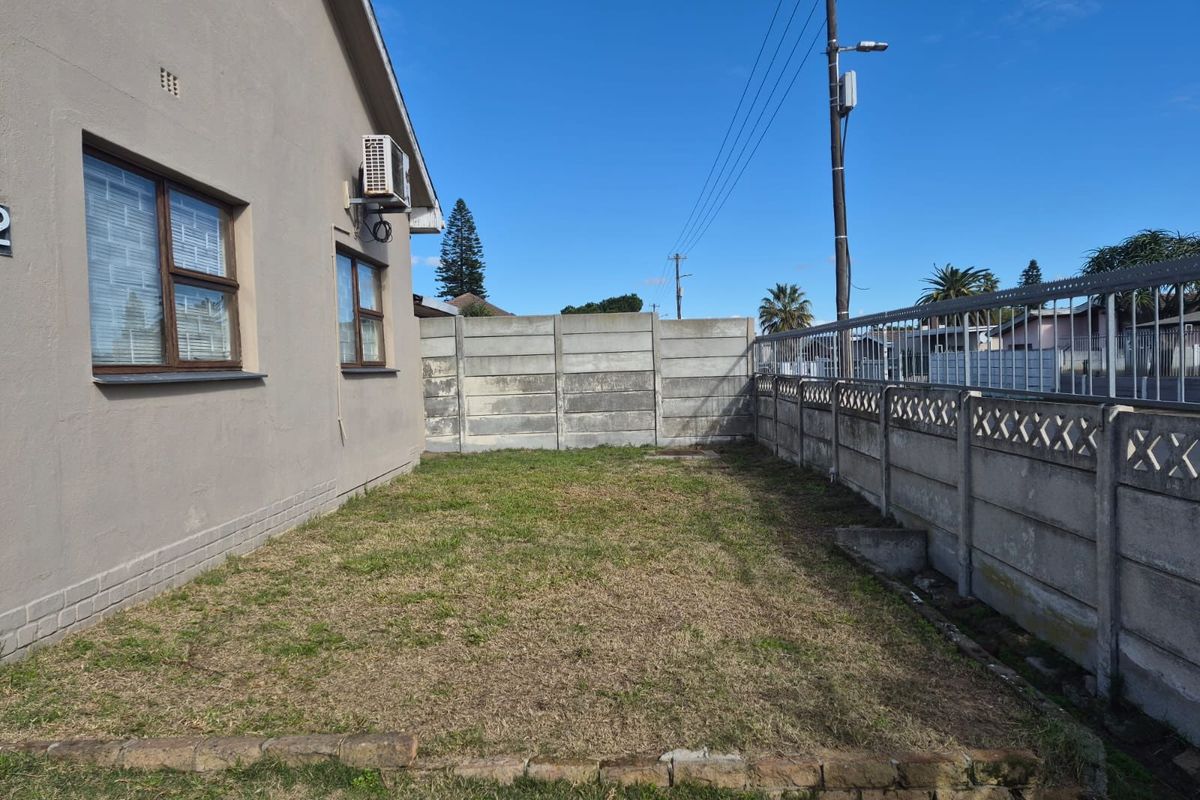 A side garden area featuring a lawn, enclosed by precast concrete boundary walls and adjacent to the house exterior with an installed air conditioning unit.