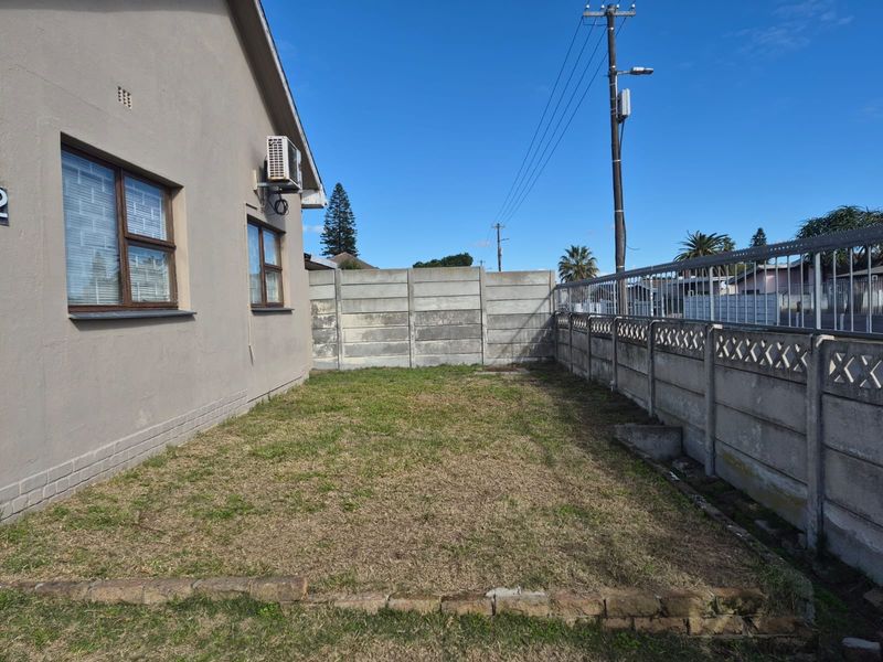 A side garden area featuring a lawn, enclosed by precast concrete boundary walls and adjacent to the house exterior with an installed air conditioning unit.