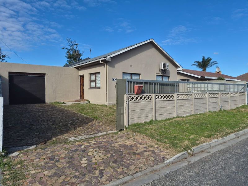 Front elevation of a single-story house featuring a paved driveway, attached garage, and a secure boundary wall with a metal gate.