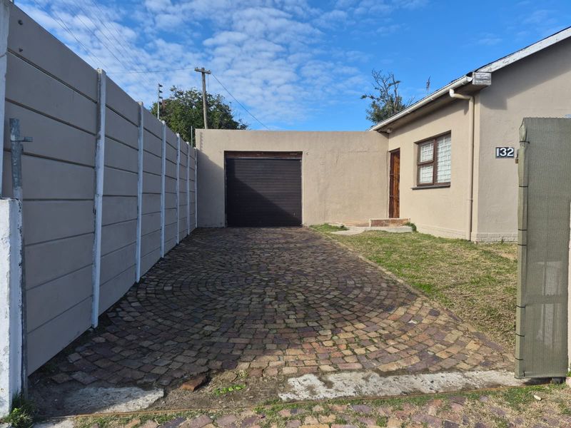 Front exterior view of the property featuring a paved driveway, single garage, and perimeter boundary wall.