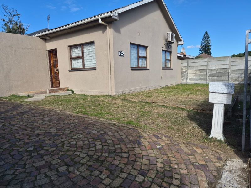 Front exterior view of a single-story house featuring a paved driveway, small front lawn, and security gate entrance.