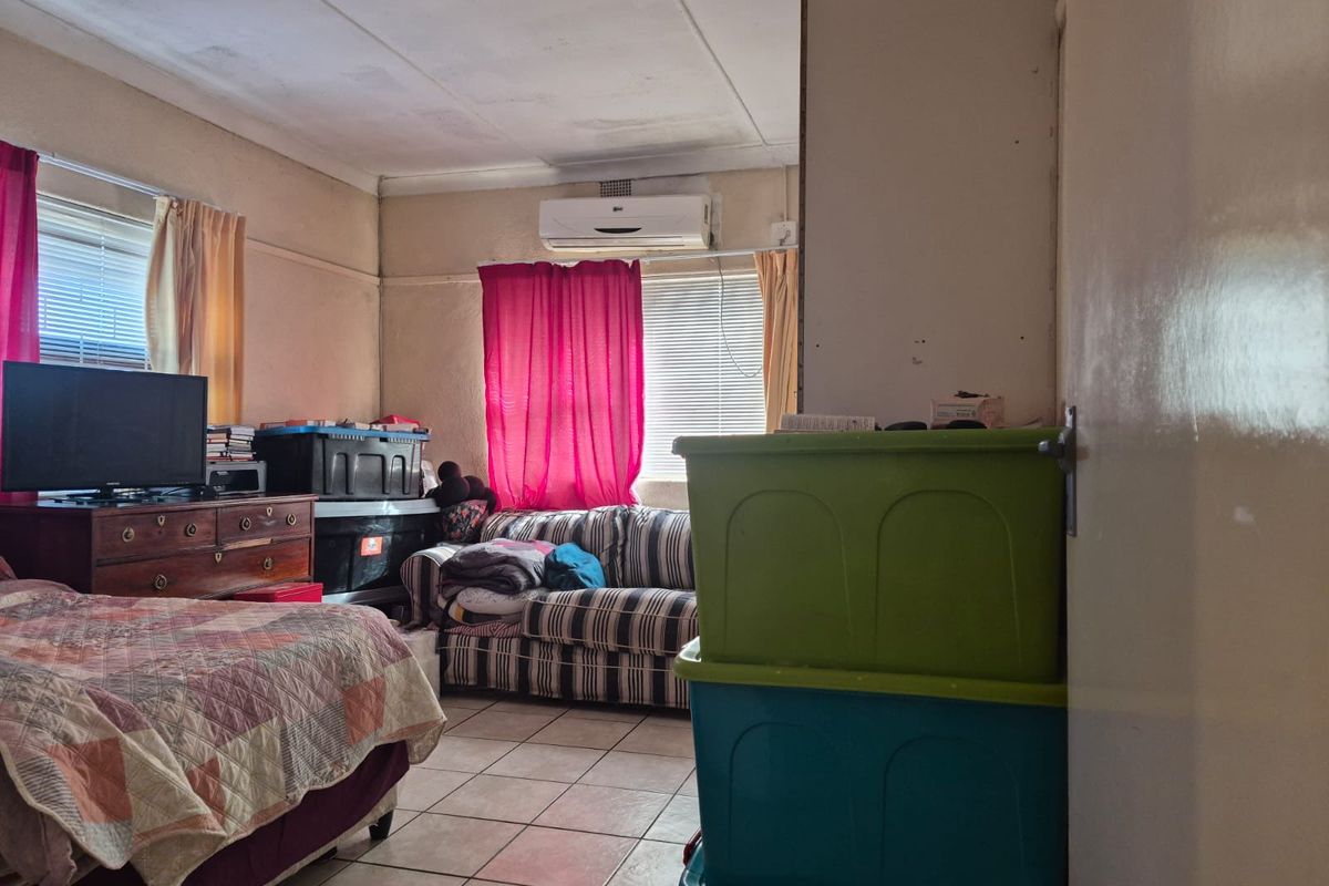 A bedroom featuring tiled flooring, a wall-mounted air conditioning unit, and large windows allowing natural light into the space.