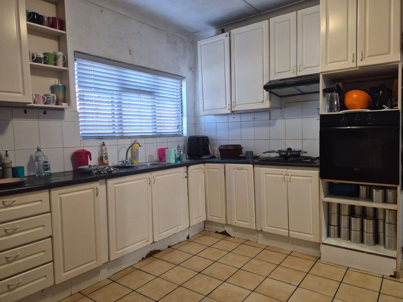 A dated kitchen featuring white cabinetry, dark countertops, a built-in oven, and tiled flooring, requiring cosmetic updates and repairs to base cabinetry.