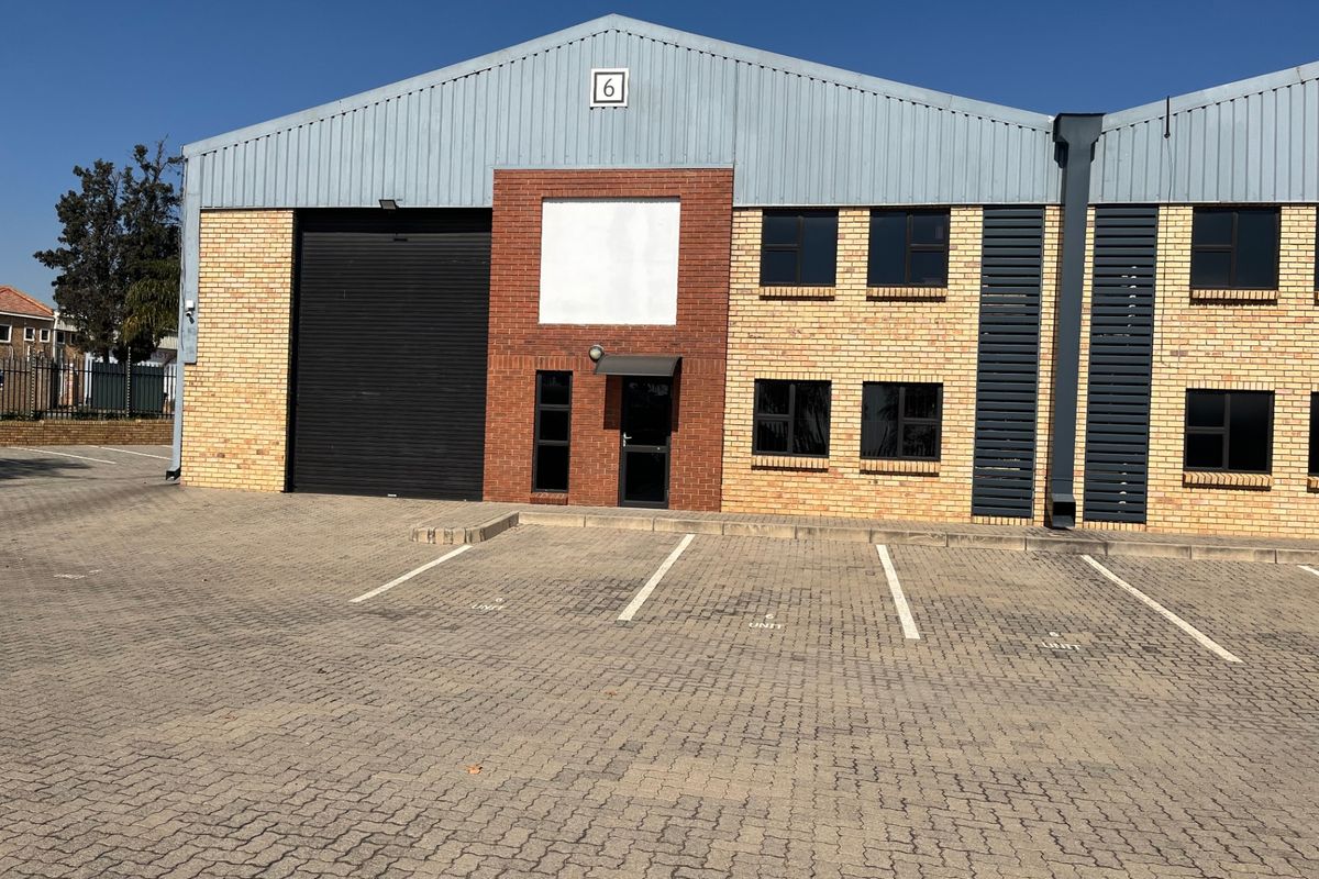 Industrial unit exterior featuring a brick facade, roller shutter door, and paved parking area in front.