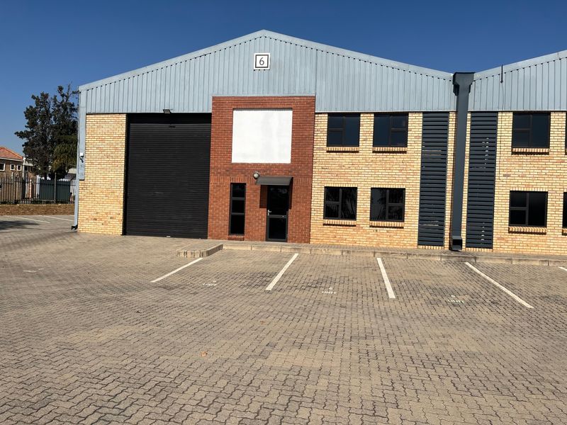 Industrial unit exterior featuring a brick facade, roller shutter door, and paved parking area in front.